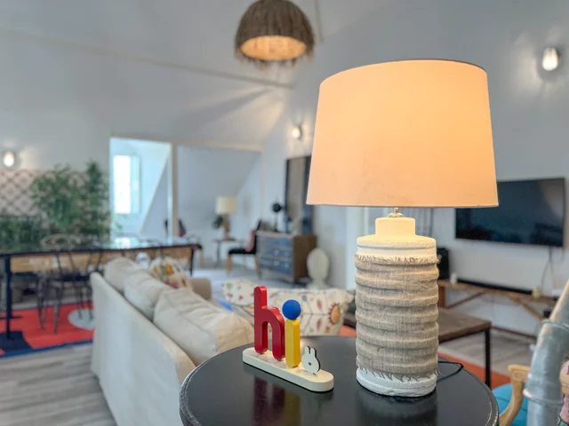 Table lamp with a textured base and a colourful wooden 'hi' sculpture, with the living room blurred in the background
