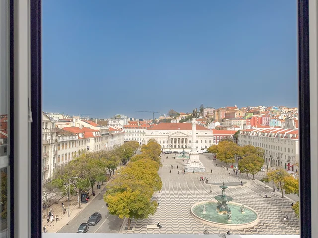 Wide view of Praça do Rossio framed by the apartment window — the square, Mar Largo cobblestones, and Pombaline buildings on both sides